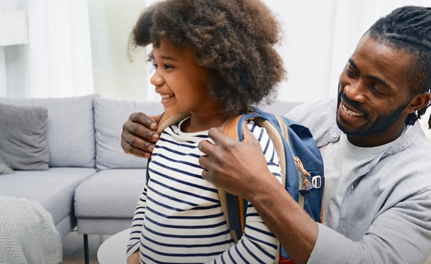 Black father helping his child put on backpack